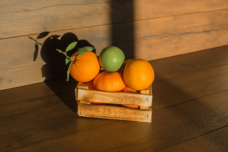 Oranges and a lime in a small wooden crate in warm evening light