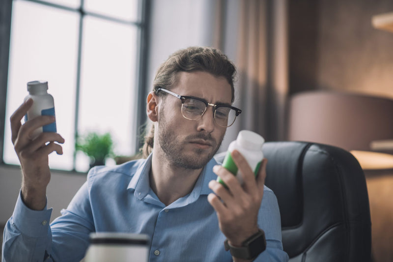 A man in glasses compares the labels on two supplement bottles