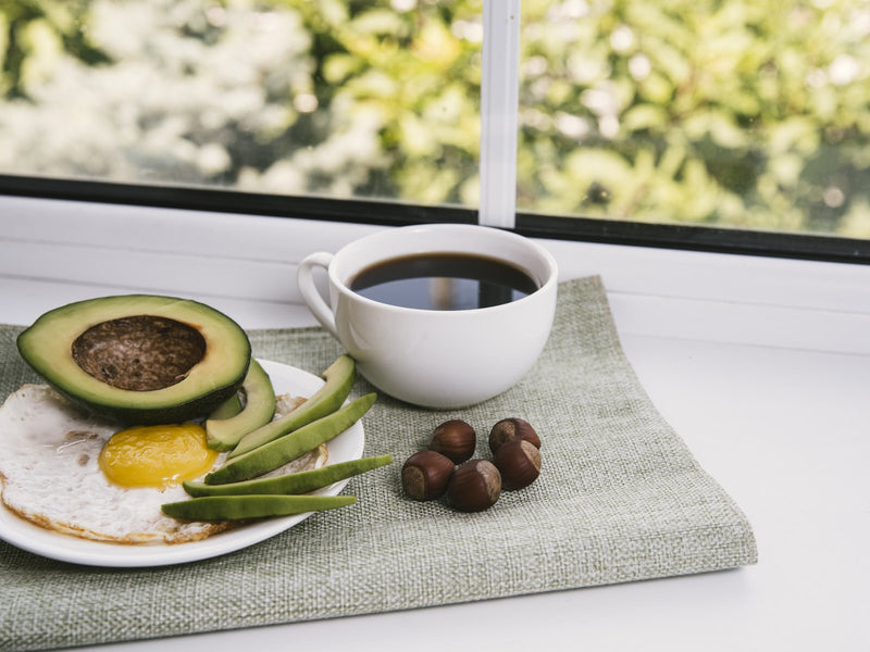 A fried egg, avocado and hazelnuts with a cup of coffee by a sunny window