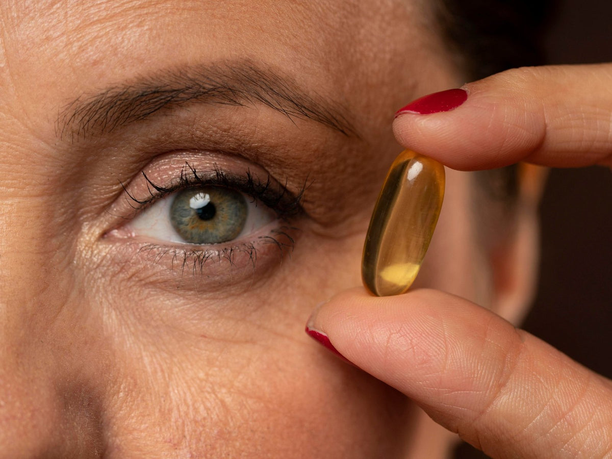 Close-up of an eye beside an omega-3 softgel held between two fingers
