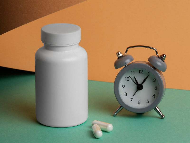 Supplement bottle and capsules beside an alarm clock