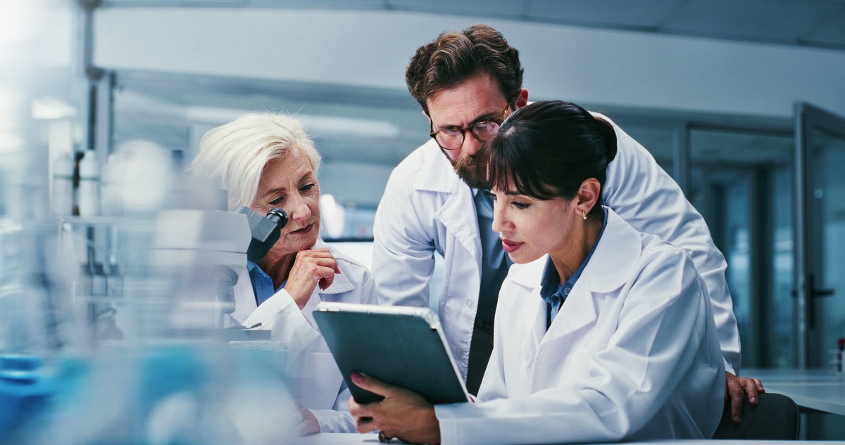 Three scientists in lab coats review research results together on a tablet in a laboratory